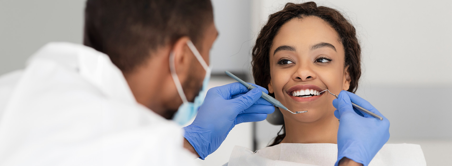 A dental hygienist is performing a teeth cleaning procedure on a smiling patient in a dentist s office.