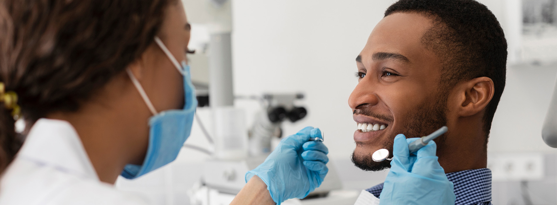 A dental professional in a lab coat and mask attending to a patient in a dental chair, with dental tools visible.