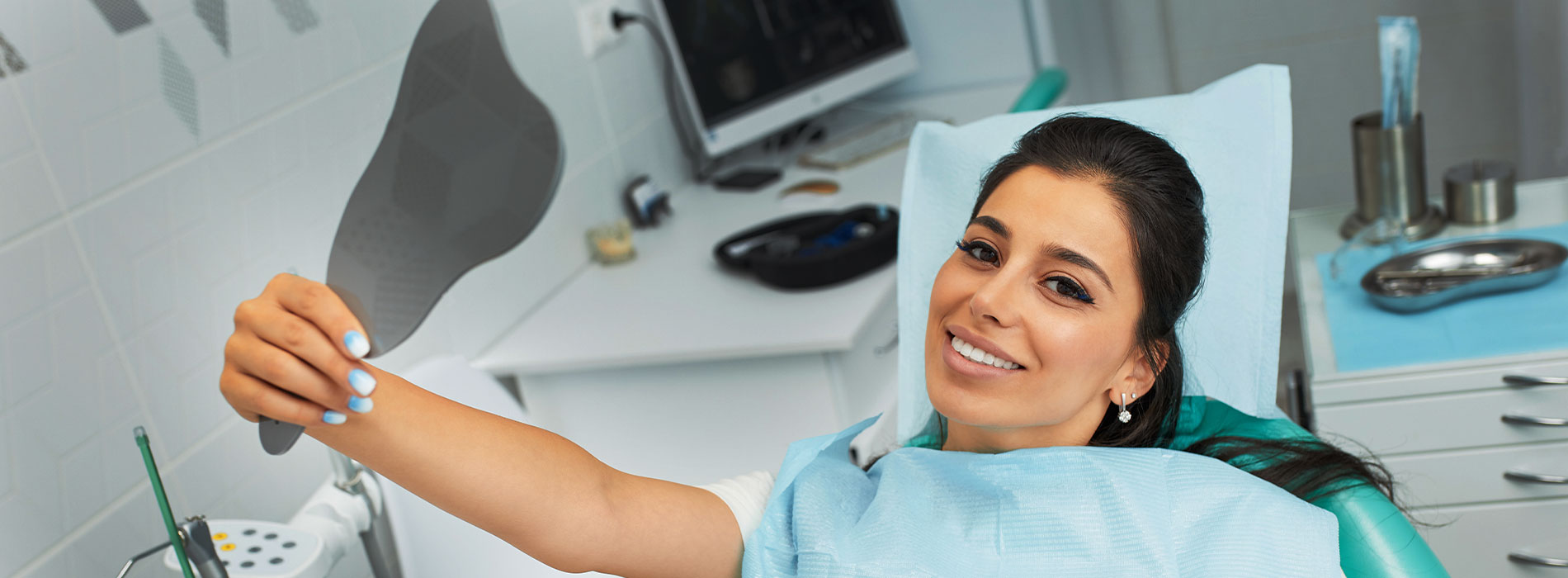 A woman in a dental office, holding up a black object that resembles a shoe, with a smiling expression.