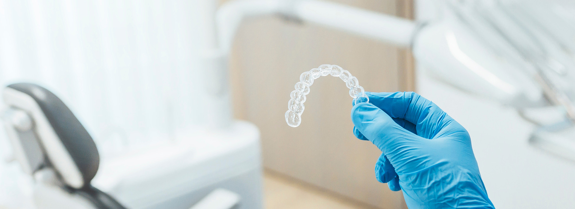 An image of a person s hand holding a transparent, liquid-like substance over a dental chair with medical equipment in the background.