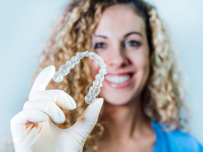 A woman in a lab coat holds up a transparent plastic dental retainer, showcasing its shape and design.