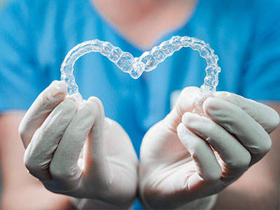 A dental hygienist s hands holding a heart-shaped clear aligner, symbolizing dental care and love.