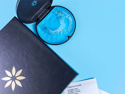 An open blue toothbrush case with a toothbrush inside, placed next to a closed black box with a gold logo and a white paper.