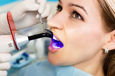 The image shows a woman receiving dental treatment, with a dentist using a device to examine her teeth.