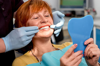 The image shows a woman sitting in a dental chair, receiving dental care.