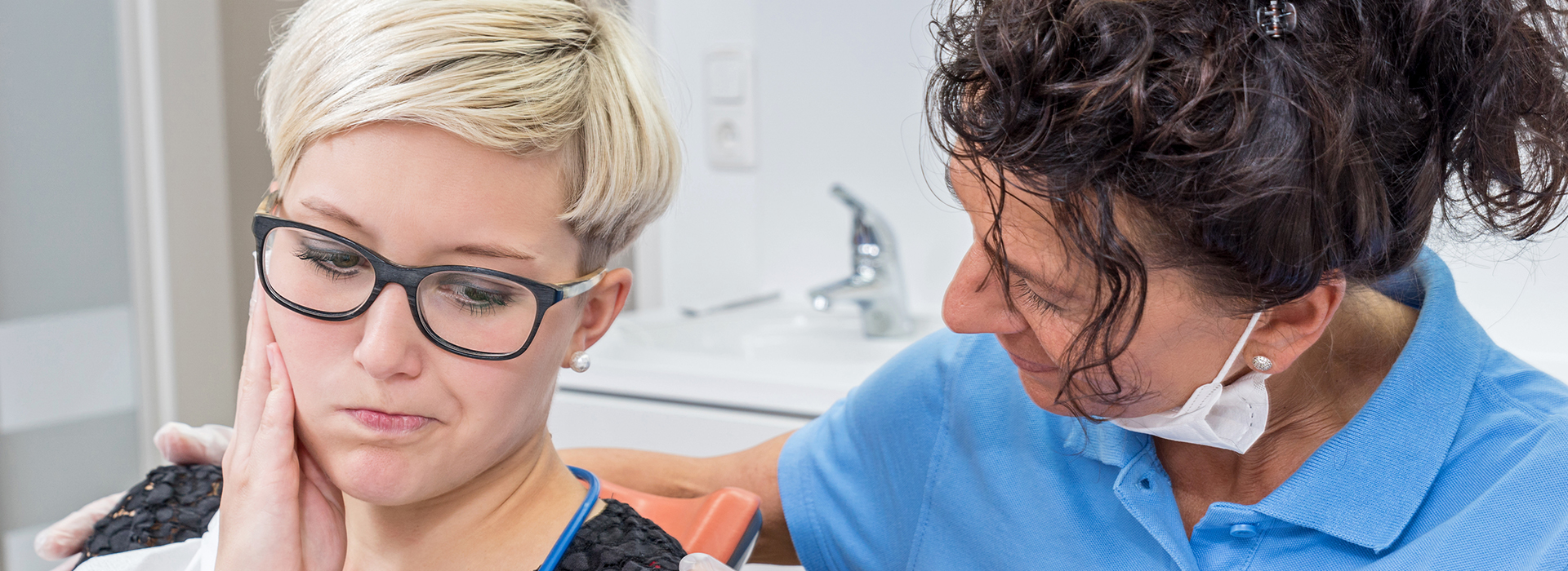 Woman in blue shirt receiving dental care from a female dentist.