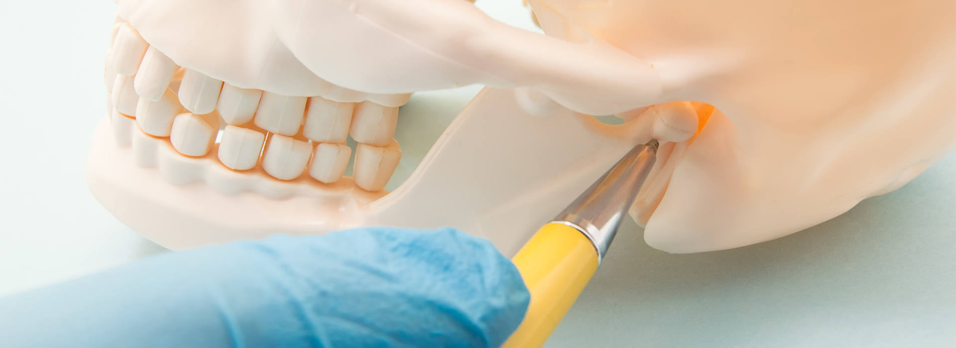 The image shows a close-up of a person s hand holding a scalpel near the edge of a tooth model, with a focus on dental implant preparation.