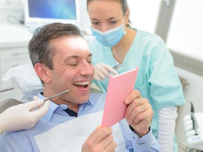 A man in a dental chair, holding up a pink card with a smile, while a dentist and hygienist attend to him.