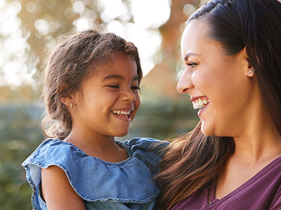 A woman and a young child smiling at the camera, with the woman holding the child.