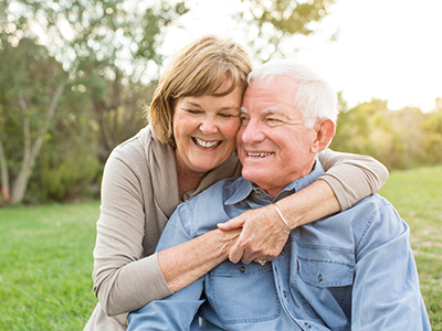 The image shows an older couple, a man and a woman, embracing each other with smiles.