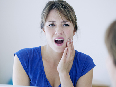 A woman with a concerned expression, holding her hand to her mouth, positioned in front of a mirror.