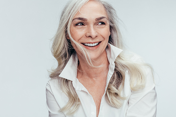 A woman with short gray hair, wearing a white top and smiling broadly at the camera.