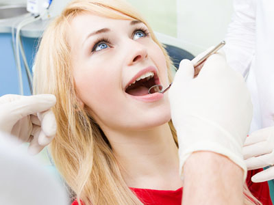 Woman in red shirt receiving dental care with open mouth, surrounded by medical professionals.