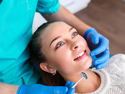 A dental hygienist performing a teeth cleaning procedure on a patient in a professional dental office setting.