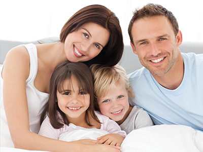 A family of four, including a man, woman, and two children, poses for a photo in bed.