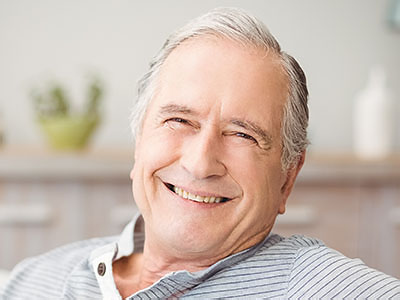 The image shows a smiling older man in a relaxed pose, likely taken from a personal photo or stock photography.